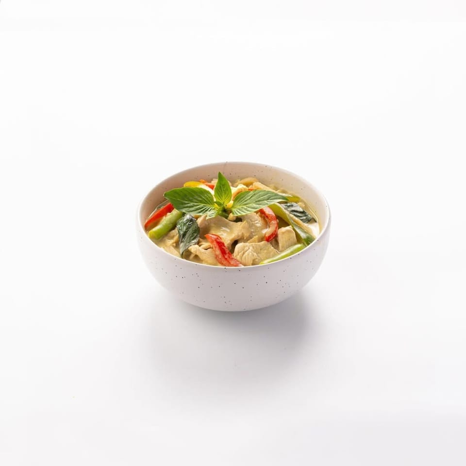 Skye Thai green curry with chicken, red bell peppers, and green beans in a white bowl.